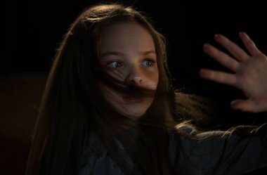 Sevimli küçük kız karanlıkta ışığa bakar ve korumak için eliyle kapatır. Çocukların korkuları, çocuk koruması ve mistisizm kavramı. Seçici odak.