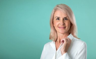 Stüdyoda yeşil bir arka planda poz veren gri saçlı, çekici yaşlı bir kadın. Makyaj ve yaşlı cilt bakımı. İş kadını gülümsüyor.