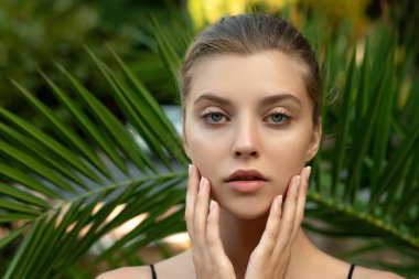 Tropikal yeşil yapraklar içinde kusursuz cilde sahip güzel genç bir kadın. Çevresel arka planda çekici model kız portresi. SPA ve sağlık, vücut bakımı ve cilt bakımı konsepti.
