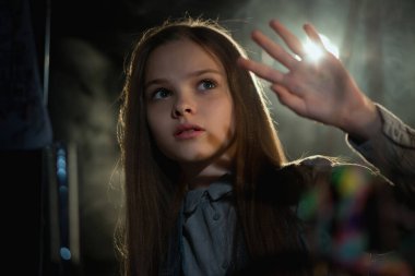 Sevimli küçük kız karanlıkta ışığa bakar ve korumak için eliyle kapatır. Çocukların korkuları, çocuk koruması ve mistisizm kavramı. Seçici odak.