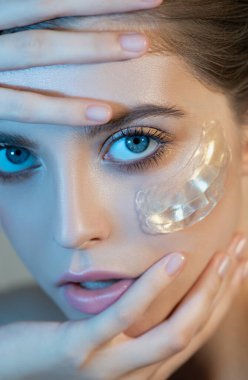 Yüzünde parlak makyaj ve altın rengi göz bantları olan güzel bir kadın yüzü, yakın plan. Doğal makyajlı bir güzellik modelinin portresi renkli stüdyo ışıklarıyla cildini önemser. Spa, cilt bakımı ve sağlık. Seçici odak.