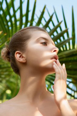 Tropikal yeşil yapraklar içinde kusursuz cilde sahip güzel genç bir kadın. Çevresel arka planda çekici model kız portresi. SPA ve sağlık, vücut bakımı ve cilt bakımı konsepti.