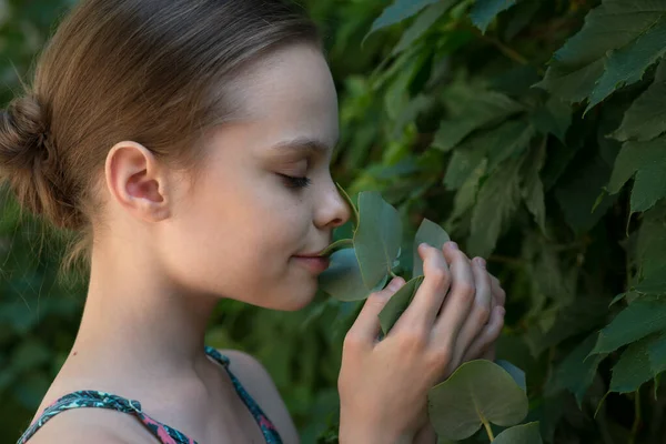 Beautiful cheerful smiling girl with eucalyptus leaf branch breathes in the scent of leaf. Child with herbal plants. Kid with clean perfect skin, SPA, skincare and wellness concept. Close up, selective focus.