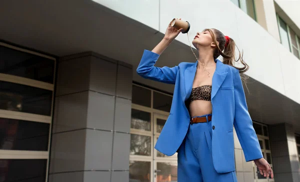 身穿蓝色西服 头戴纸杯外卖咖啡的年轻貌美女子在城市街道上跳舞 时尚模特与一杯咖啡 胜利概念 — 图库照片