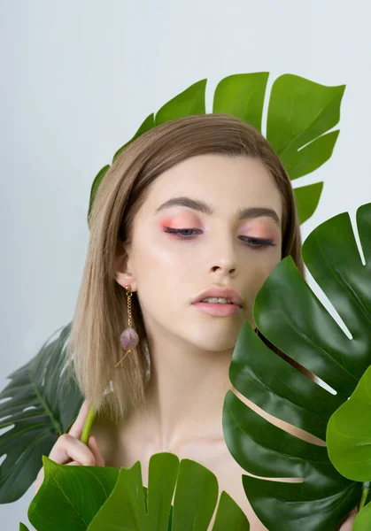 Beautiful young woman with perfect skin and natural make up posing front of plant tropical green leaves background. Teen model are of her face and body. SPA, wellness, bodycare and skincare.