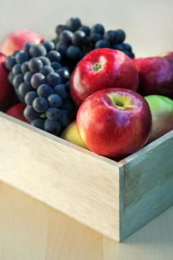 Apples and grapes in a wooden box, close up, selective focus clipart