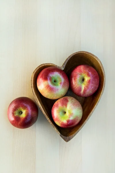Jabłka w serce drewniane kształt płytki na stole, z bliska — Zdjęcie stockowe