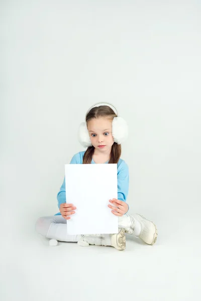 Leuk meisje in winter kleding met een witte blanco papier blad. — Stockfoto