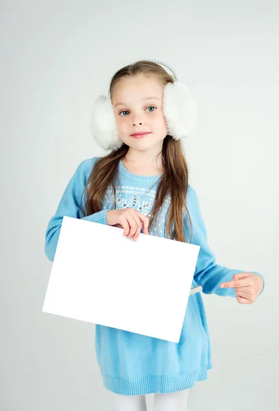 Leuk meisje in winter kleding met een witte blanco papier blad. — Stockfoto