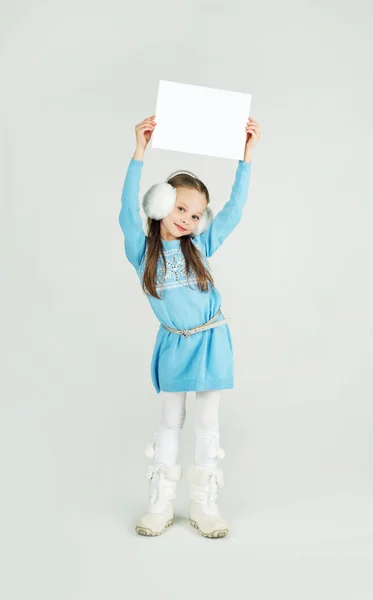 Menina bonito em roupas de inverno com uma folha de papel em branco . — Fotografia de Stock