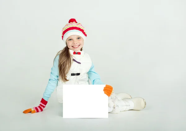 Cute girl in winter clothes with a white blank paper sheet. — Stock Photo, Image