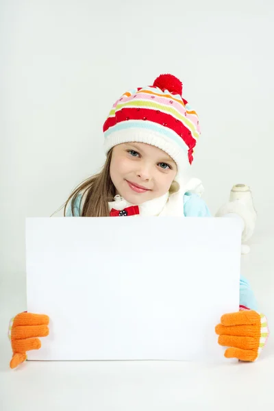 Cute girl in winter clothes with a white blank paper sheet. — Stock Photo, Image