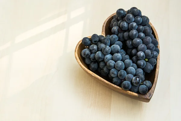 Druiven in een hart vorm houten plaat — Stockfoto