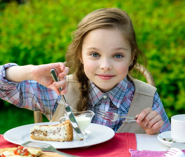 Cute little girl sitting by dinner table and eating — Stock Photo, Image