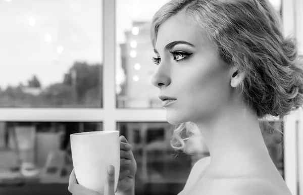 Красивая молодая женщина с кофе или чай кружку перед окном — стоковое фото