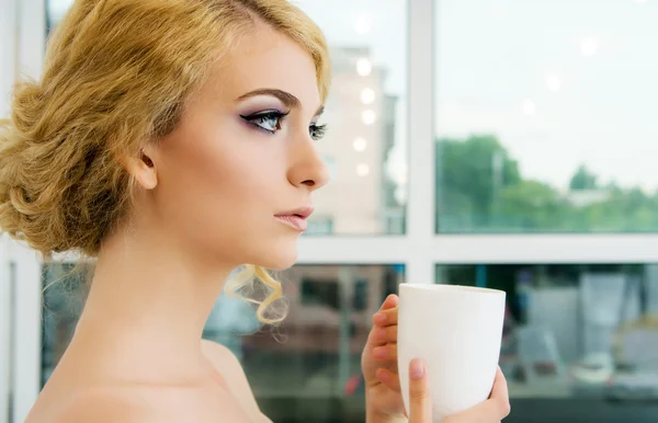 Gyönyörű fiatal nő, kávé vagy tea bögre elöl az ablak — Stock Fotó