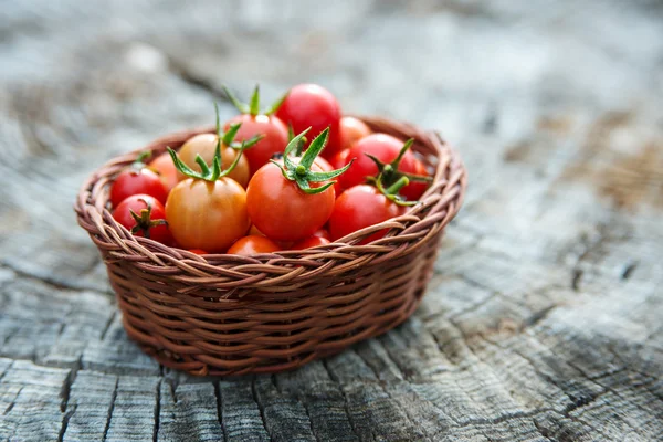 Tomates cereja em uma pequena cesta em uma superfície de madeira velha — Fotografia de Stock