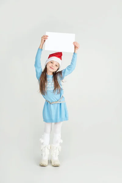 Cute girl in Santa Claus hat with a white blank paper sheet. — Stock Photo, Image