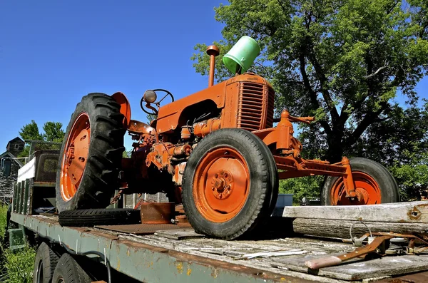 Stary traktor pomarańczowy na płaskim łóżku ciężarówka — Zdjęcie stockowe