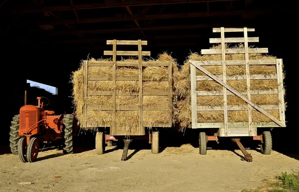 Orange tractor and hayracks full of straw bundles — Stock Photo, Image