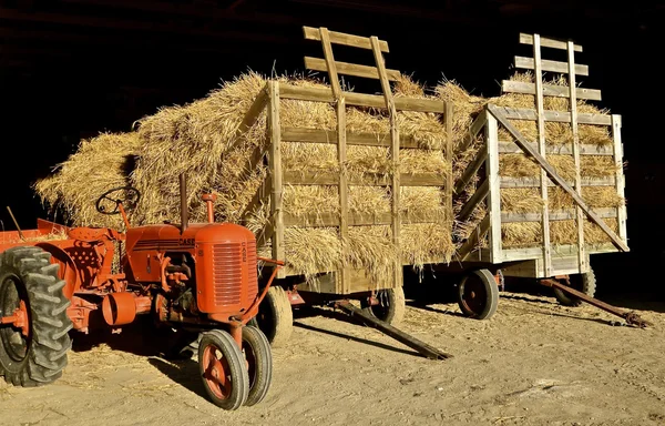 Starý traktor věci zaparkované u hayracks ze slámy — Stock fotografie
