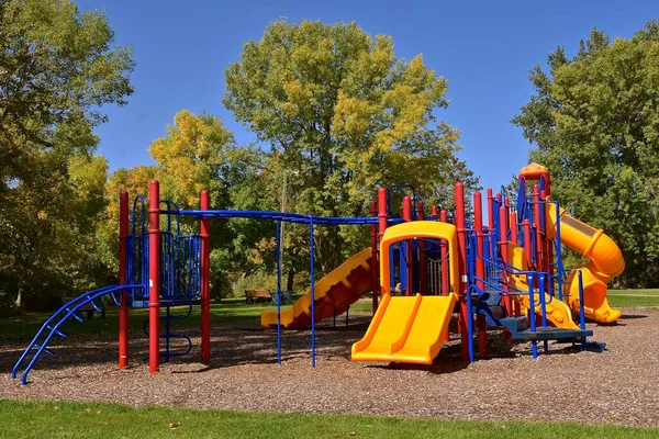 Yapraklı arka planda sonbahar renklerine dair ilk ipucunun bulunduğu bir parkta yeni renkli oyun alanı ekipmanı