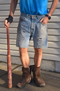 İş kıyafetleri ve botları olan kimliği belirsiz bir adam ve eski ahşap beyzbol sopası.