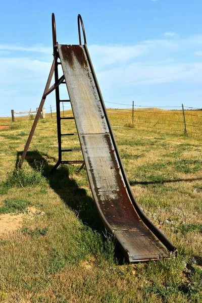 古い金属製の滑りやすいスライドは 農村西部の草原の設定で遊び場に残っています — ストック写真