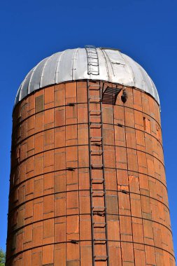 Çok eski kahverengi bir taş silo, merdiveni ve teneke çatısı var..
