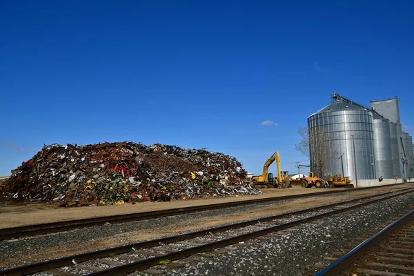 A huge pile of scrap metal and iron  adjacent to railroad tracks ready to be loaded.