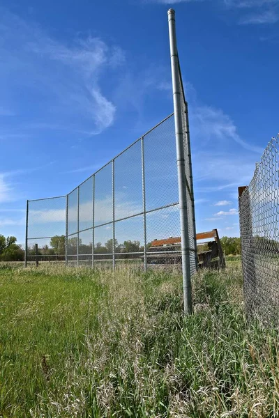 A crumbling bleacher rests behind the screened  backstop of home plate in a rural setting.