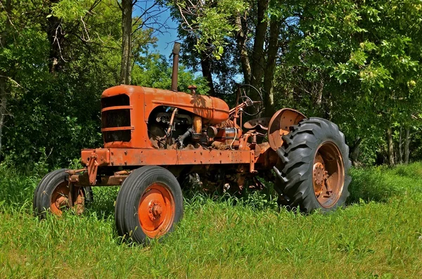 Orangefarbener alter Traktor steht in der Nähe eines Baumhains — Stockfoto