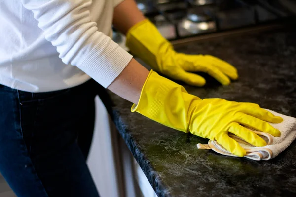 Γυναίκα νοικοκυρά καθαρίζει το σπίτι με κίτρινα γάντια σκουπίζει τη σκόνη από το τραπέζι της κουζίνας πάνω στο πιάτο Εικόνα Αρχείου