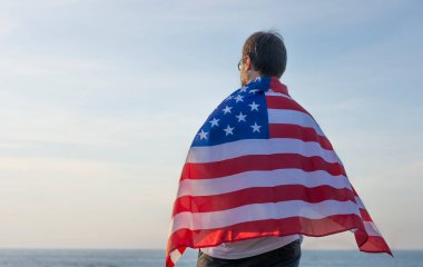 Deniz ve gökyüzünün arka planında Amerikan bayrağı taşıyan genç adam