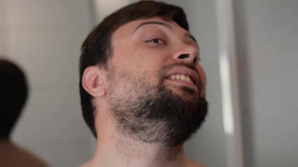 Joven hombre guapo con barba mira a la cámara y sonríe — Vídeo de stock