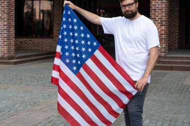 Gözlüklü, sakallı, Amerikan bayrağı taşıyan ve Bağımsızlık Günü 'nü kutlayan genç yakışıklı bir adam.