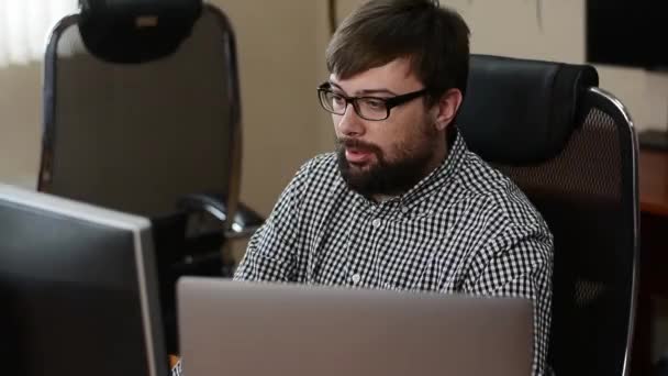 Närbild porträtt av attraktiv brunhårig man sitter på jobbet vid datorn — Stockvideo