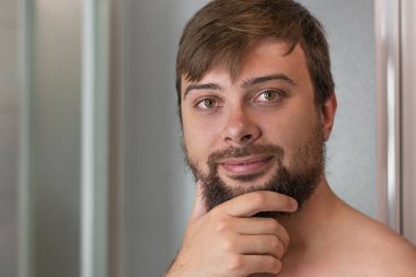 Sakallı genç yakışıklı adam banyodaki kameraya bakıyor.
