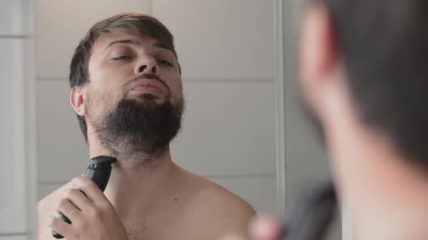 Joven hombre guapo con barba mira a la cámara y sonríe — Vídeo de stock