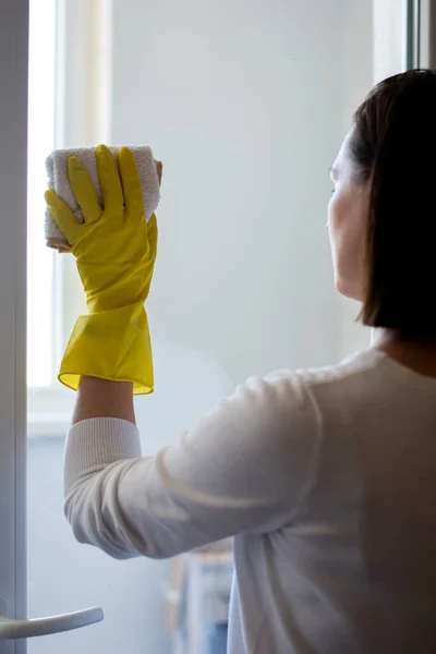 Hausfrau wäscht Glas in ihrer Wohnung mit gelben Gummihandschuhen und weißem Lappen — Stockfoto