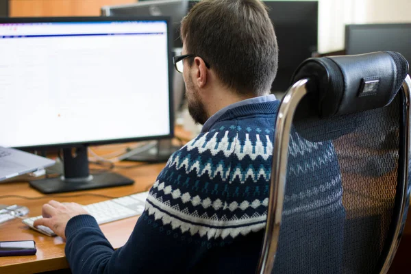 Genç programcı, ahşap bir masada, iki monitörün önünde serbest çalışan beyaz bir klavyede daktilo kullanıyor.
