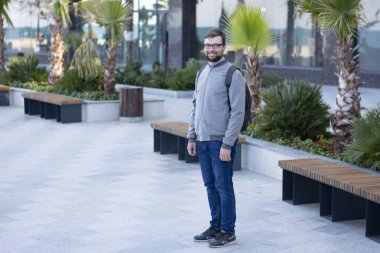 Gri ceketli, sakallı ve gözlüklü bir adam arka planda duruyor.