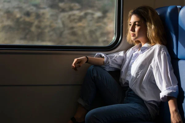 Κορίτσι επιβάτης που ταξιδεύει με τρένο κάθεται στο κάθισμα και κοιτάζει έξω από το παράθυρο Φωτογραφία Αρχείου
