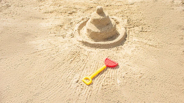 Sandcastle on the blue sea in summertime and toy shovel — Photo