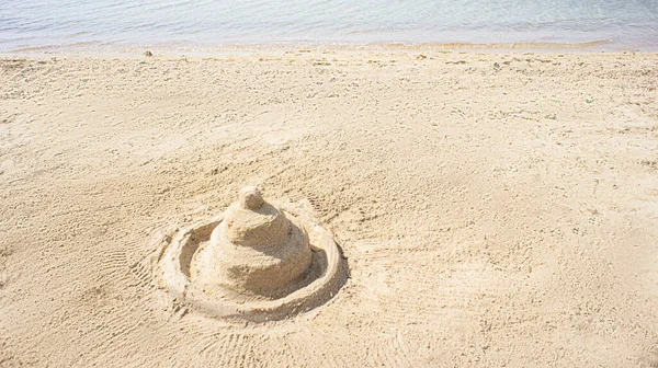 Holiday concept with sandcastle on sandy beach against a summer sky and blue sea — Photo