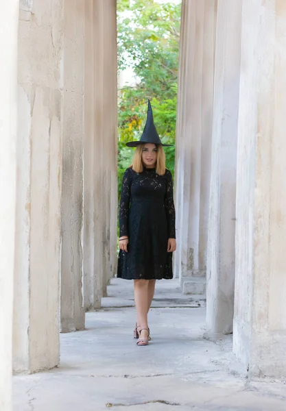 Retrato completo de mujer hermosa en traje de bruja negro para halloween con sombrero sobre fondo gris —  Fotos de Stock