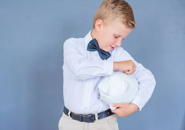 Primer plano retrato elegante niño poniendo moneda de dinero en la alcancía sobre un fondo azul —  Fotos de Stock