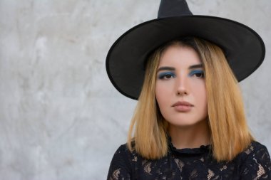 Cadılar Bayramı cadı kostümlü, gri arka planda şapkası olan mutlu gotik genç kadın.