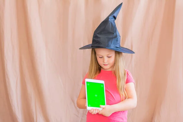 Retrato de una chica en un sombrero de bruja con una maqueta verde pantalla de la tableta espacio de copia de Halloween —  Fotos de Stock