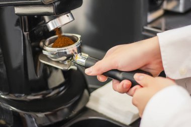 Kafedeki bir barista tarafından öğütücüye dökülen taze kahvenin yakın plan çekimi.